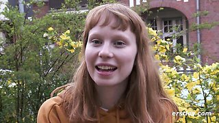 Redhead with bangs talks outdoors in bright orange hoodie by yellow flowers